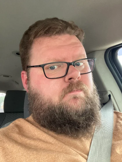 Tyler Woodward, bearded and wearing dark-rimmed glasses.